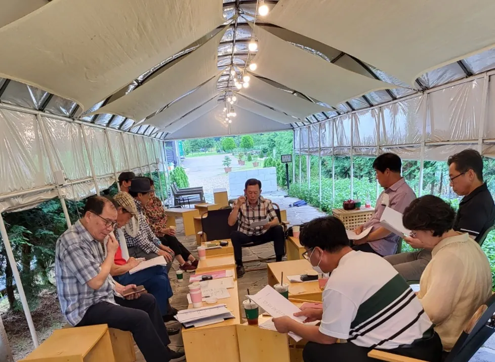 편백 토요 아카데미 합평 모습 — 회원들이 텐트 안에서 원고를 펴 들고 서로의 글을 읽고 있다
